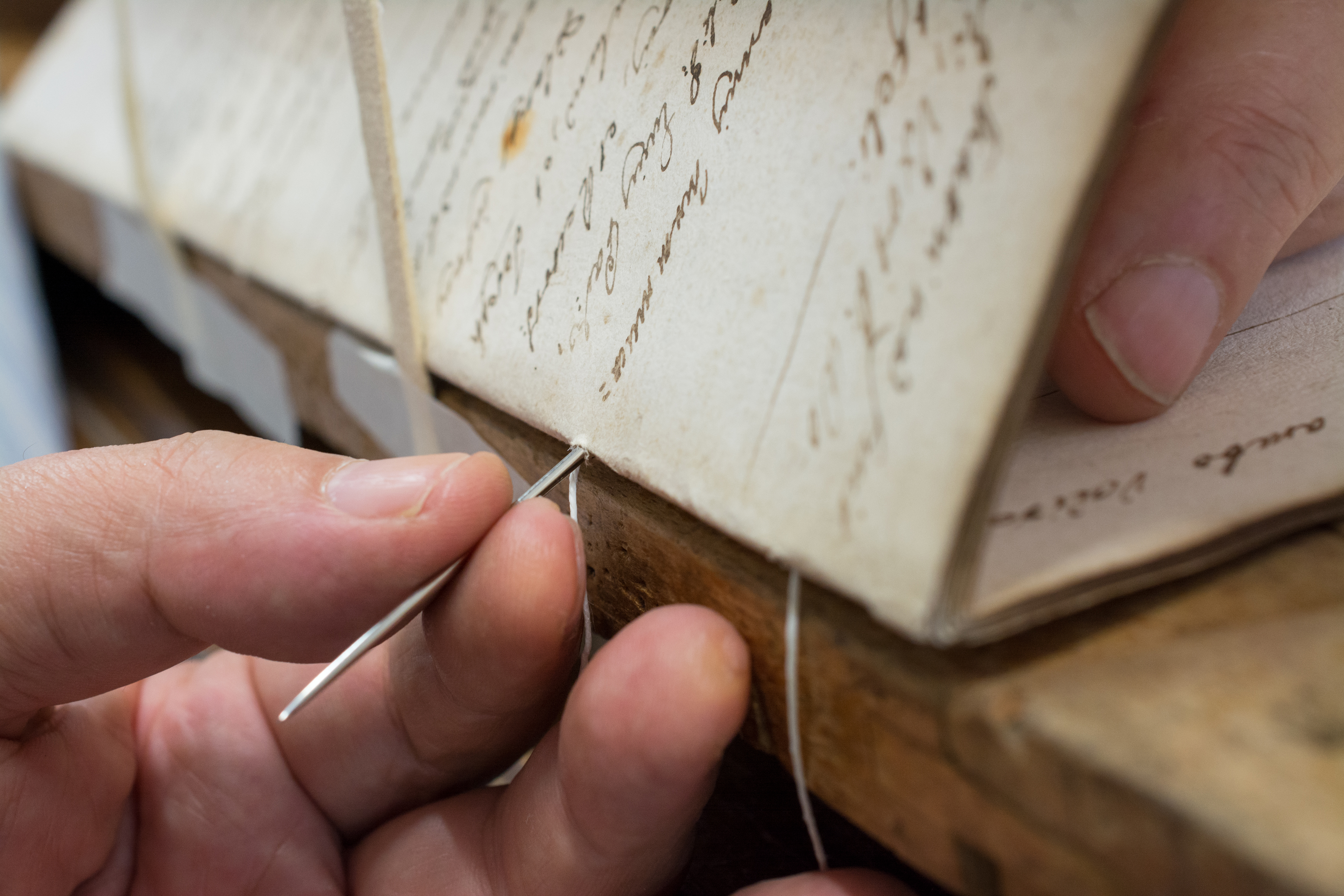 Hands binding a manuscript with needle and thread — knowledge made permanent and accessible